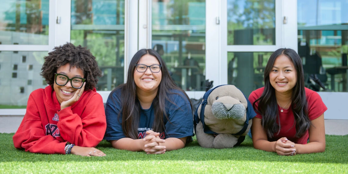 3 young women posing on the lawn with Hugh the Manatee