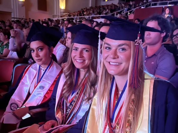 Three graduates in cap and gown at ceremony